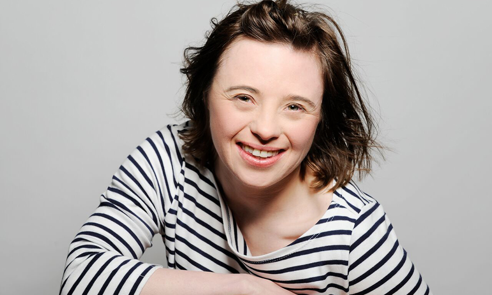 British actor Sarah Gordy is dressed in a top with black and white stripes and is posing for the camera with a big smile