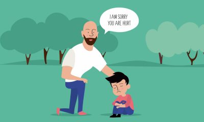 An illustration of a father and son in a park. The father, dressed in a white t-shirt and blue pants, is seen kneeling down, with his arm on his son's shoulder and telling his son "I am sorry you are hurt" in a speech bubble. The son is clad in an orange t-shirt and blue pants and has a cut on his knee through which he is bleeding.