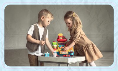 A photo of a young boy and girl stacking legos on a table together. The photo is set against a patterned, light blue backdrop