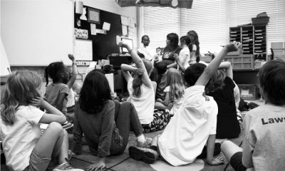 A black and white image of students raising hands in a class.